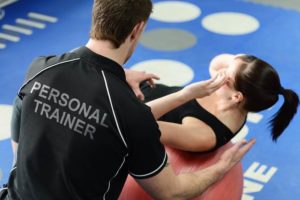 Personal trainer helping young woman in gym with crunching exercises